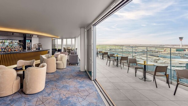 A modern lounge area with a bar, comfortable seating, and a view of an airport.