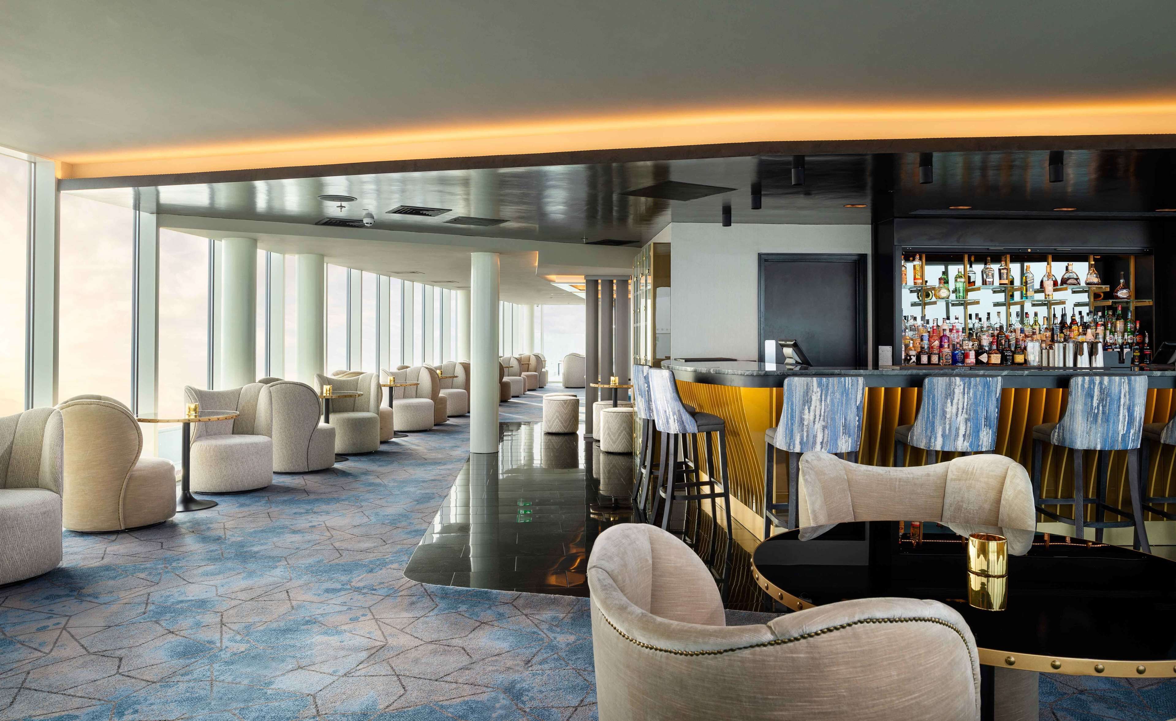 A modern bar area with a long counter, bar stools, and a variety of bottles.