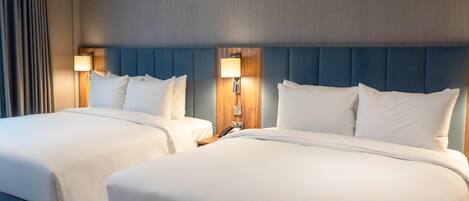 A hotel room with two beds, a wooden headboard, a lamp, and a telephone on the nightstand.