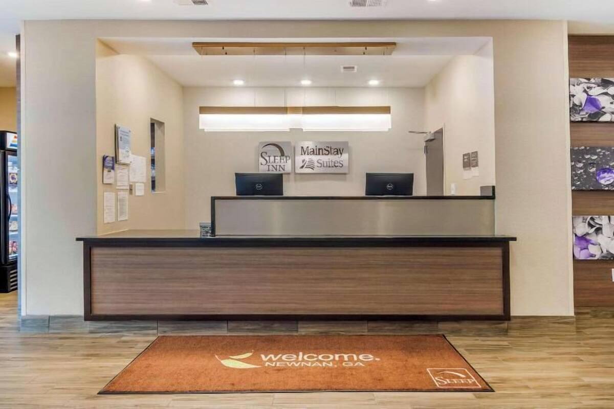 A reception desk with a 'Welcome' mat, 'Sleep Inn' and 'MainStay Suites' signs, and a wall-mounted bulletin board.