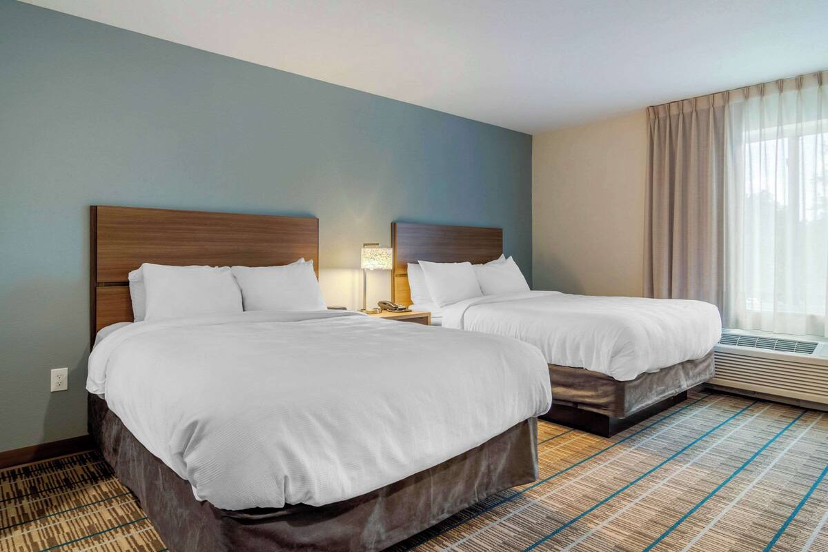 A hotel room with two beds, a nightstand, a lamp, and an air conditioning unit.