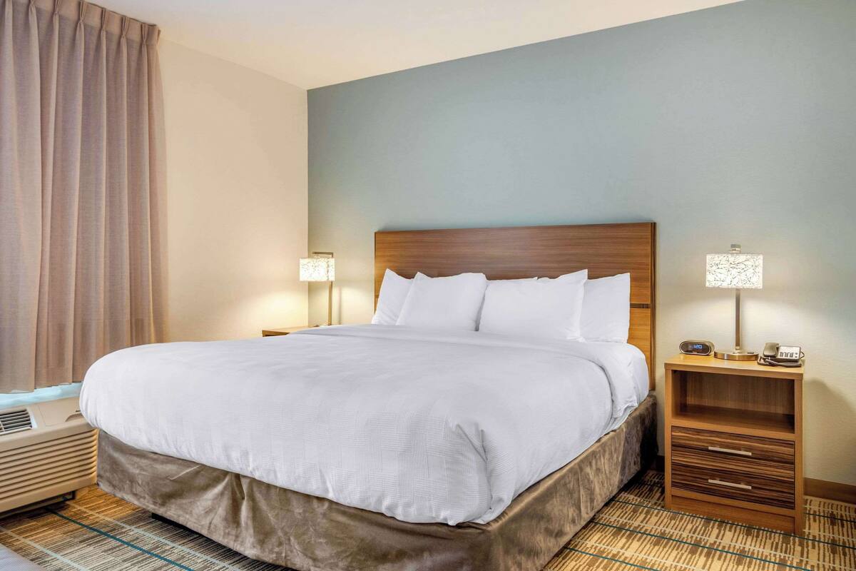 A hotel room with a large bed, two bedside tables, a nightstand, and a wall-mounted lamp.