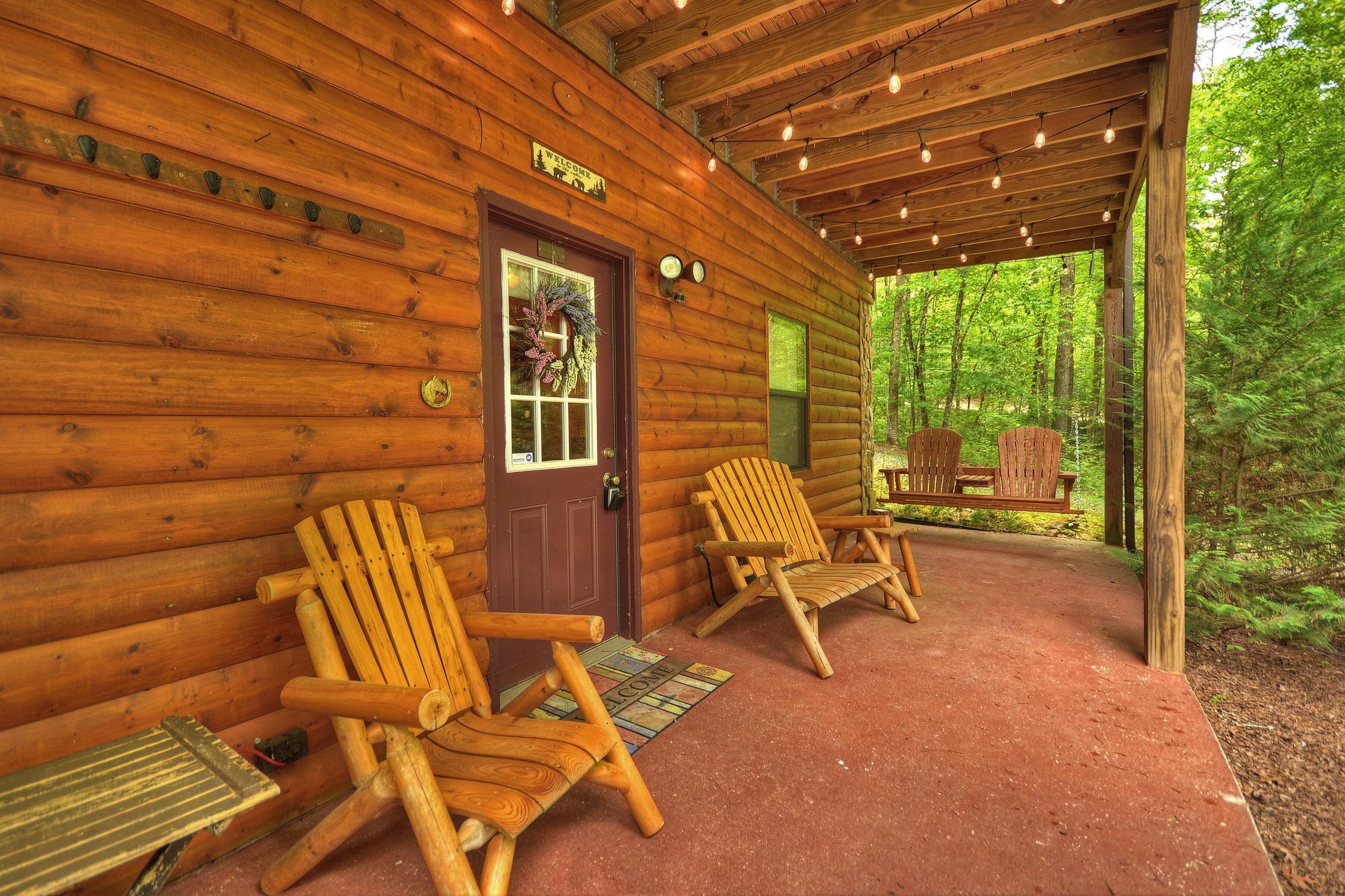 Een houten chalet met twee Adirondack stoelen buiten, een overdekte veranda en een welkomstbord.