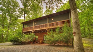 A wooden cabin with a balcony, surrounded by trees and gravel.