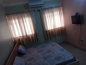 Un dormitorio con cama, cortinas, aire acondicionado y televisor.