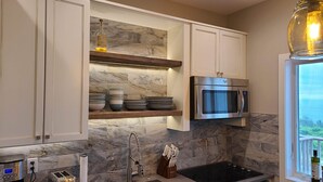 Una cocina moderna con armarios blancos, horno empotrado, microondas, lavaplatos con grifo moderno y ventana con vistas.