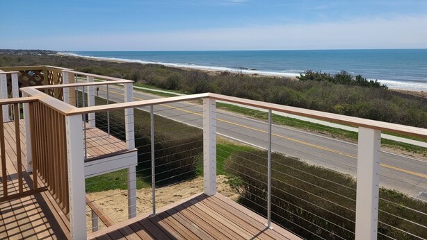 Una terraza de madera con baranda metálica que da a una playa y una carretera.