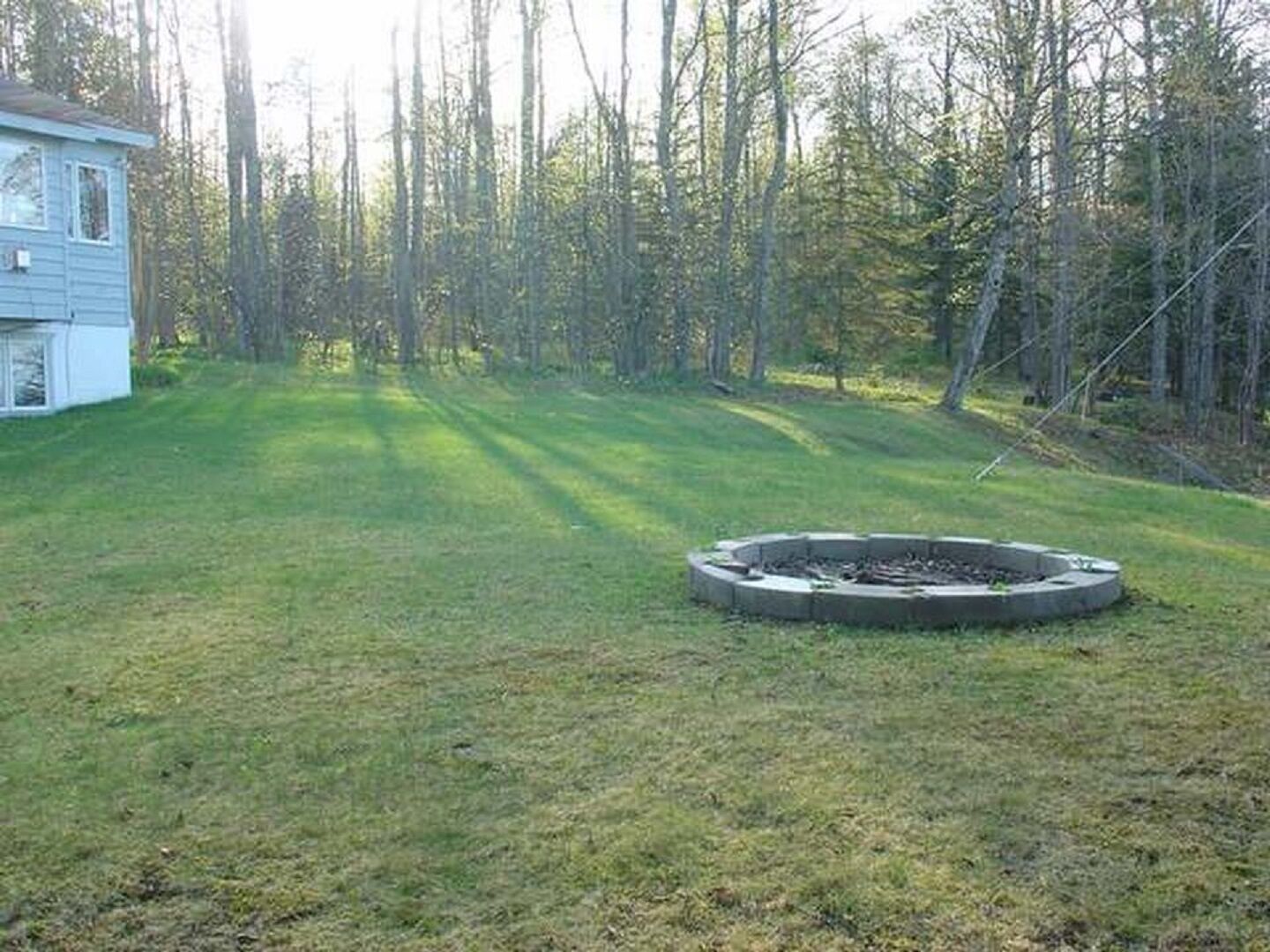 A backyard with a circular fire pit, a lawn, and a house in the background.