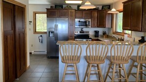 Una cocina con armarios de madera, electrodomésticos de acero inoxidable, un refrigerador, un microondas, una estufa y una barra con tres sillas de madera.
