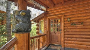En stuga av trä med en björnstaty på verandan, en trädörr och en välkomstskylt.