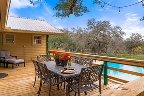 A wooden deck with a table and chairs, a small house with a metal roof, and a pool in the background. - The Country Life Experience, Close to Distilleries, Wineries, and Wedding Venues (Johnson City `)