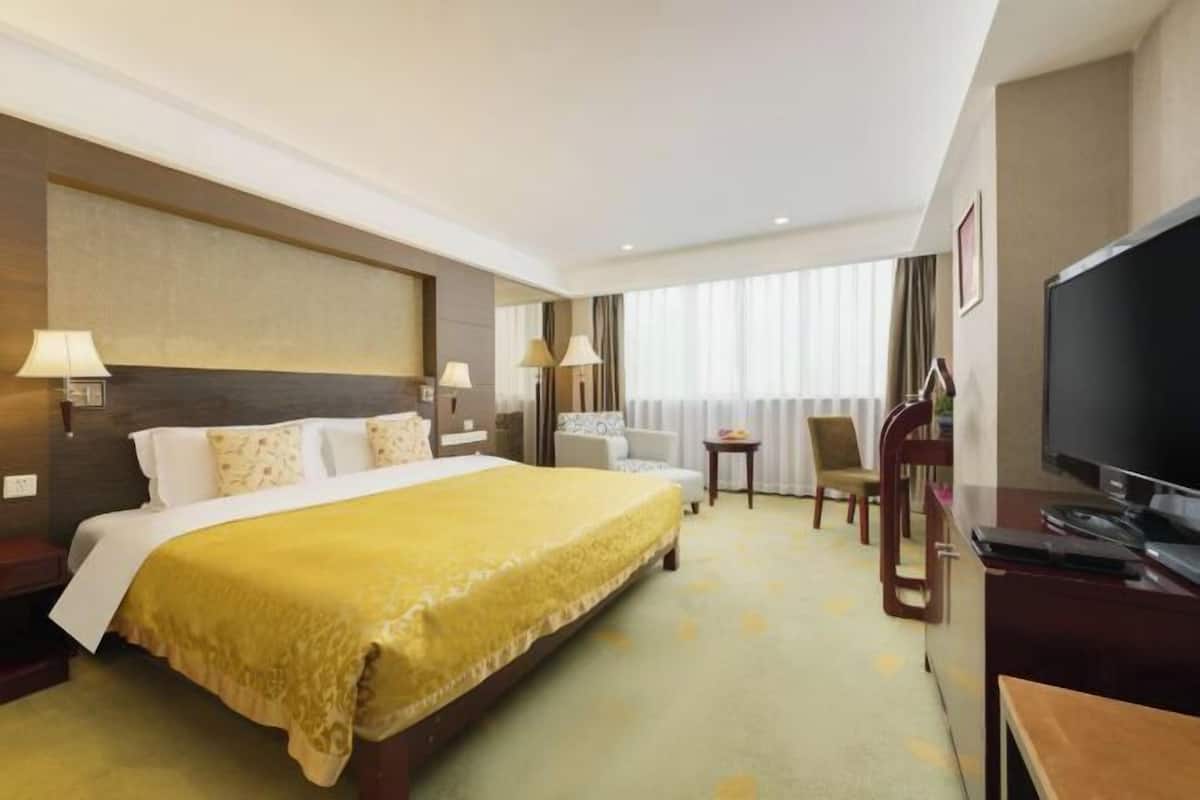 Une chambre d’hôtel avec un grand lit, un bureau avec une télévision, une chaise et une petite table.