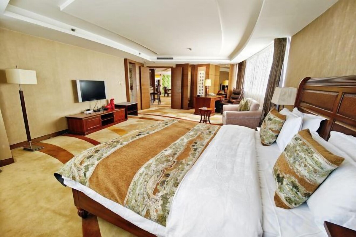 Habitación de hotel con una cama grande, un escritorio, un televisor y vista al pasillo.