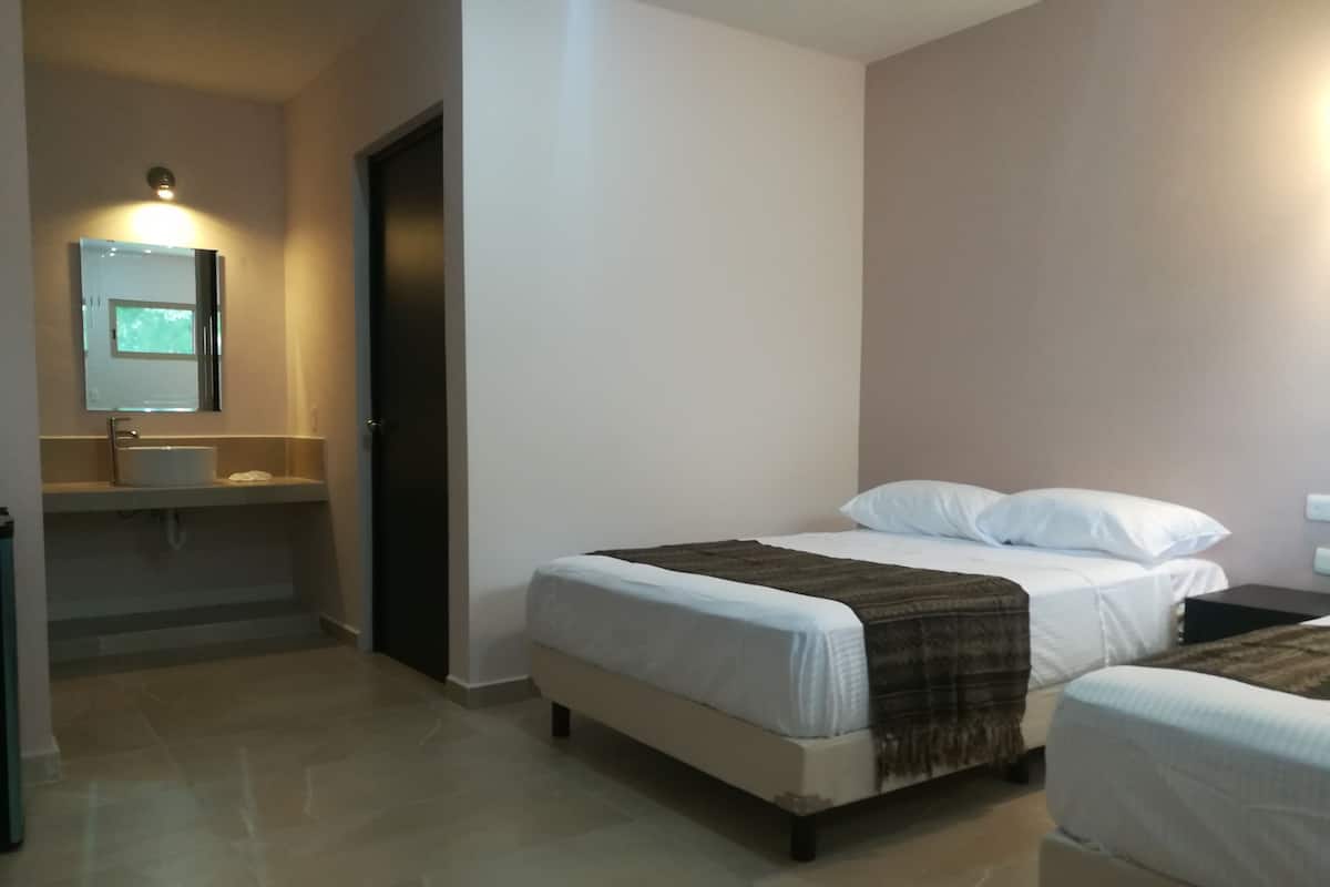 A hotel room with a bed, a bedside table, a mirror, and a bathroom with a sink and toilet.