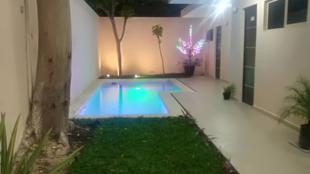 A courtyard with a swimming pool, a tree, and a building with a balcony. - Hotel Virreyes (Mérida)