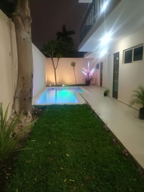Un patio con piscina, un árbol y un edificio con balcón.