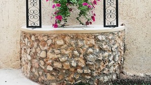 A stone planter with a metal archway and hanging light fixture, containing pink flowers. - Hotel Virreyes (Mérida)