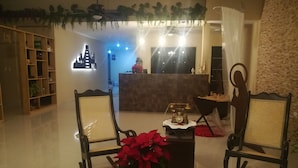 A reception area with a reception desk, two wooden chairs, a potted plant, and a decorative wall. - Hotel Virreyes (Mérida)