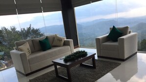 A modern living room with a sofa and armchair facing a large window overlooking a mountainous landscape. - Akway Resort (Beragala)