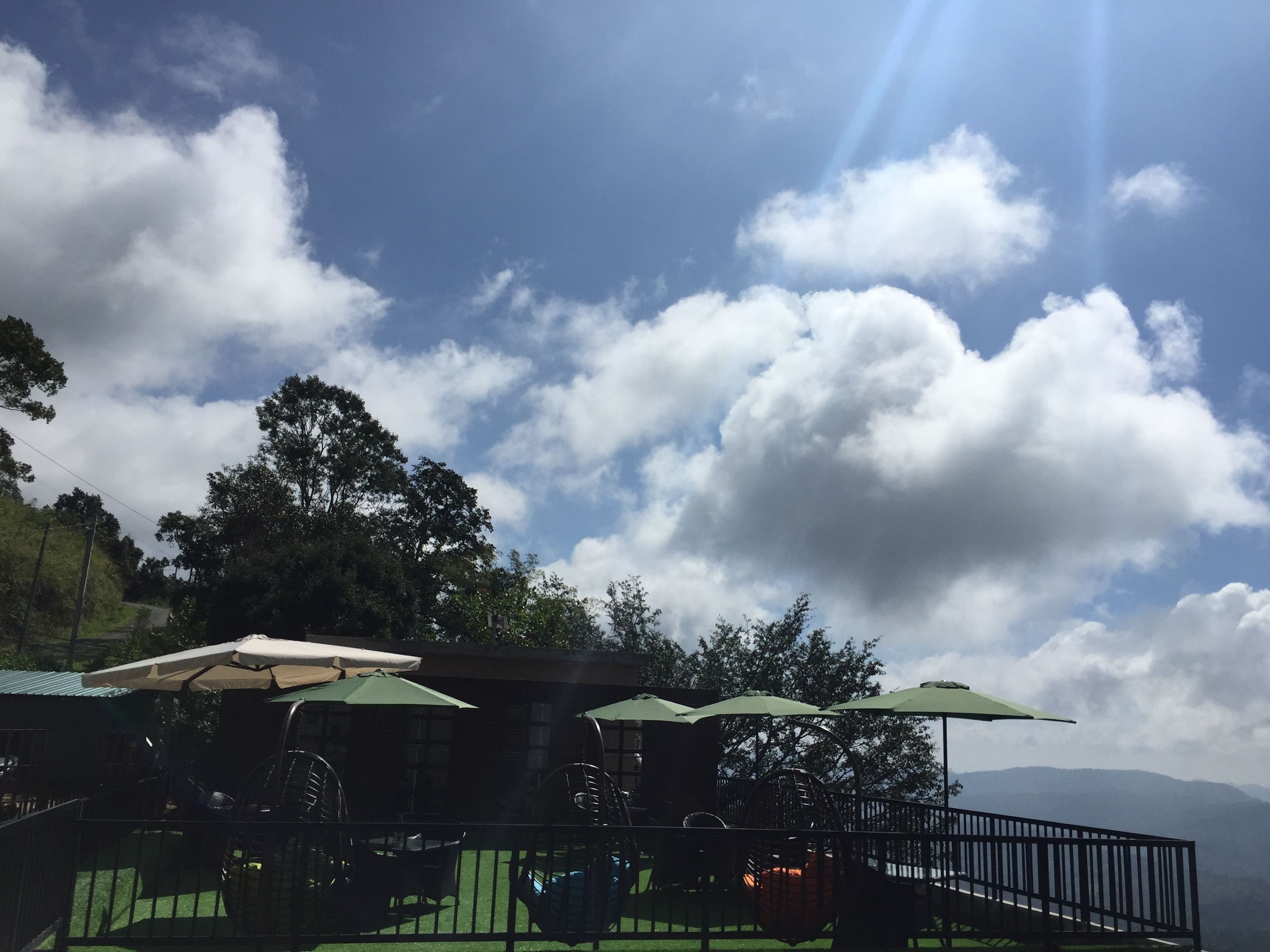 A terrace with outdoor seating, surrounded by greenery and a mountainous backdrop.