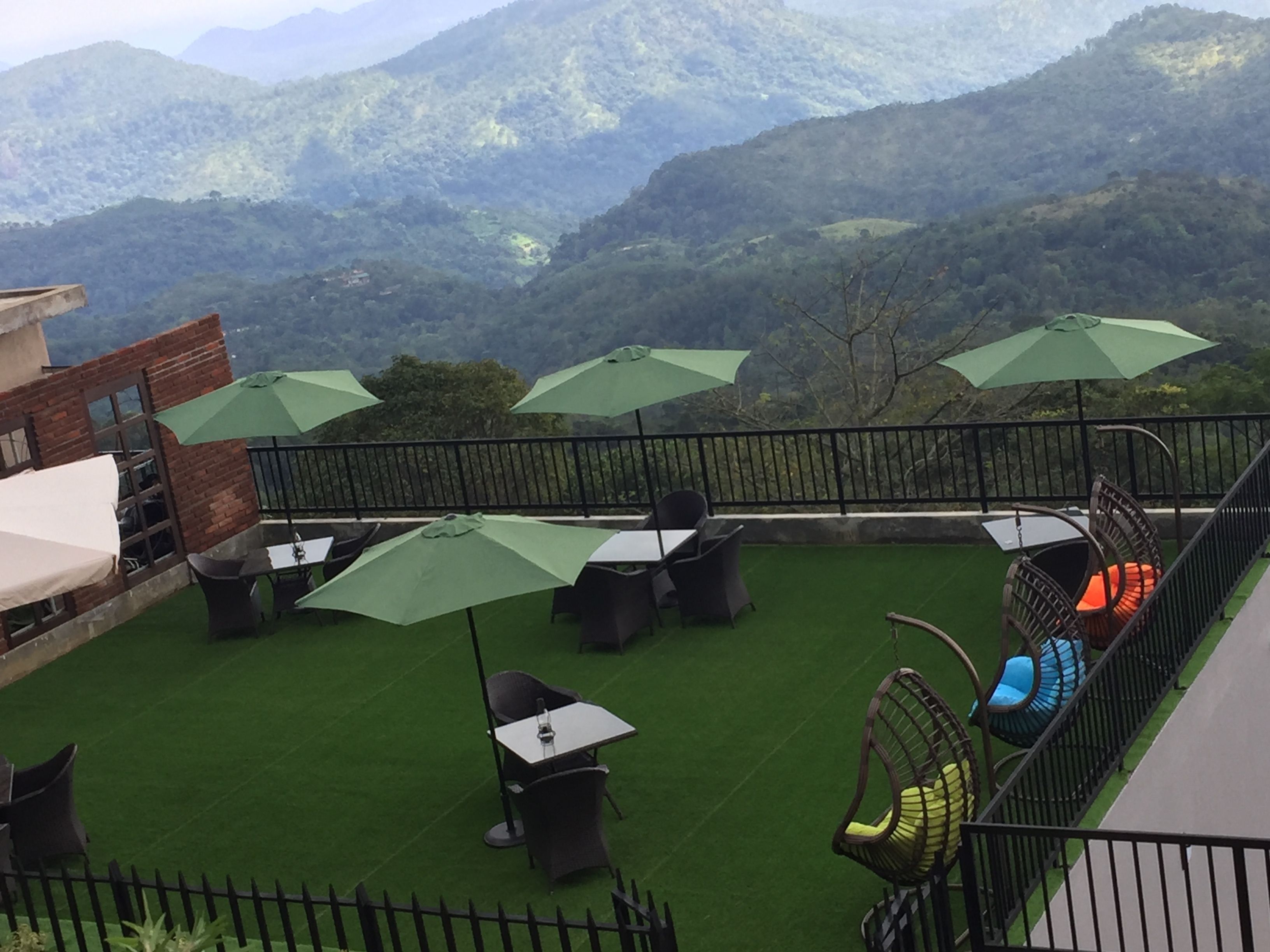 Een terras met buitenplaatsen, groene parasols en uitzicht op bergen.