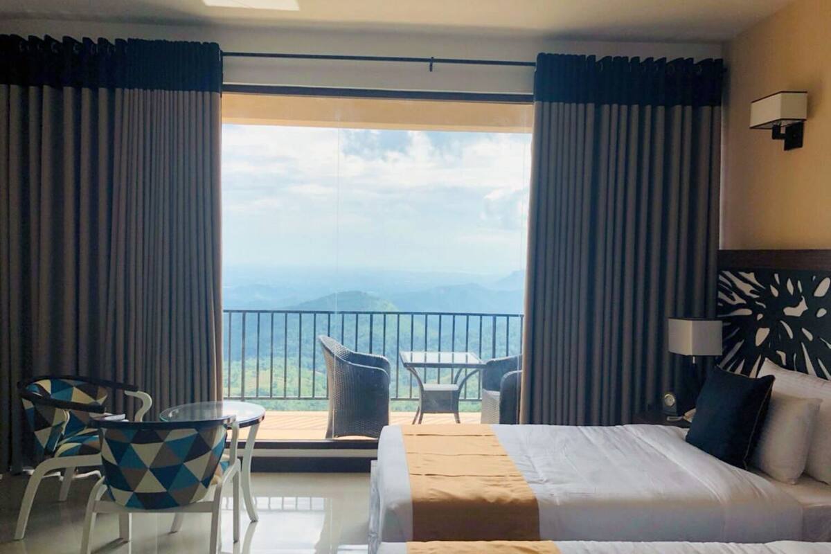 A hotel room with a bed, a table with chairs, a view of the mountains, and a balcony.