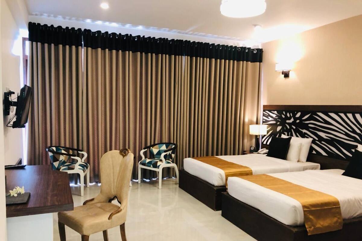 A hotel room with a bed, two bedside tables, a desk, a chair, and a large window with curtains.