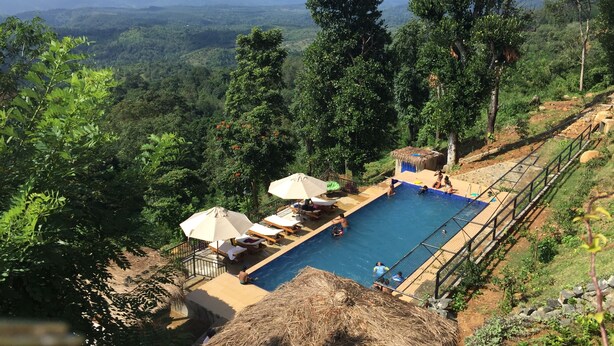 A pool area with lounge chairs and umbrellas, surrounded by lush greenery and overlooking a mountainous landscape. - Akway Resort (Beragala)