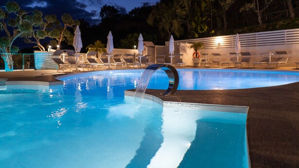 A swimming pool with a waterfall feature, lounge chairs, and umbrellas. - Relais Freedom Club (Massa Lubrense)