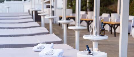 Een rij witte ligstoelen met handdoeken, een fles champagne en glazen op een tafel.