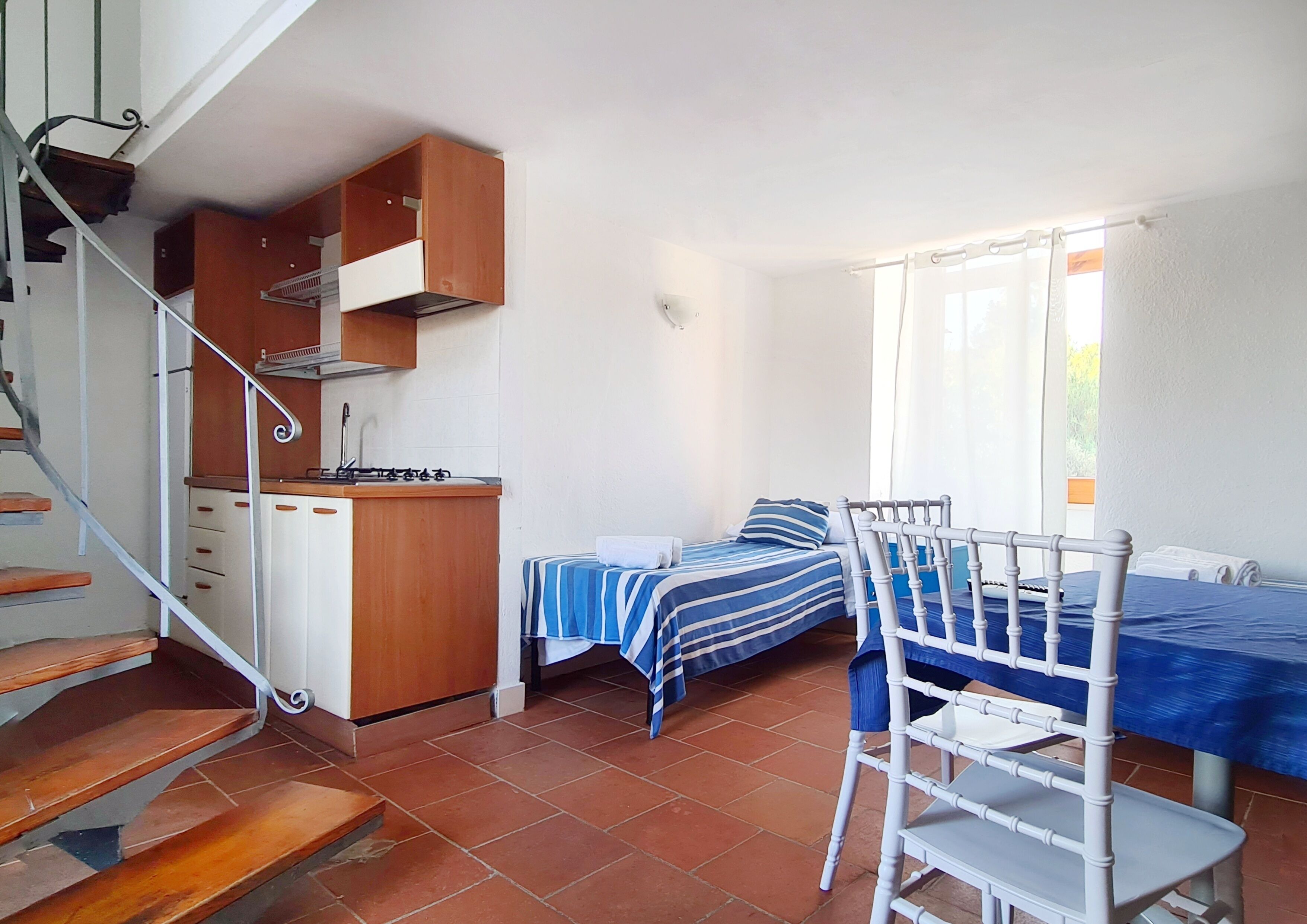 Una habitación compacta con cocina, una cama con colcha a rayas y una silla.