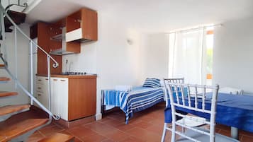 Una habitación compacta con cocina, una cama con colcha a rayas y una silla.