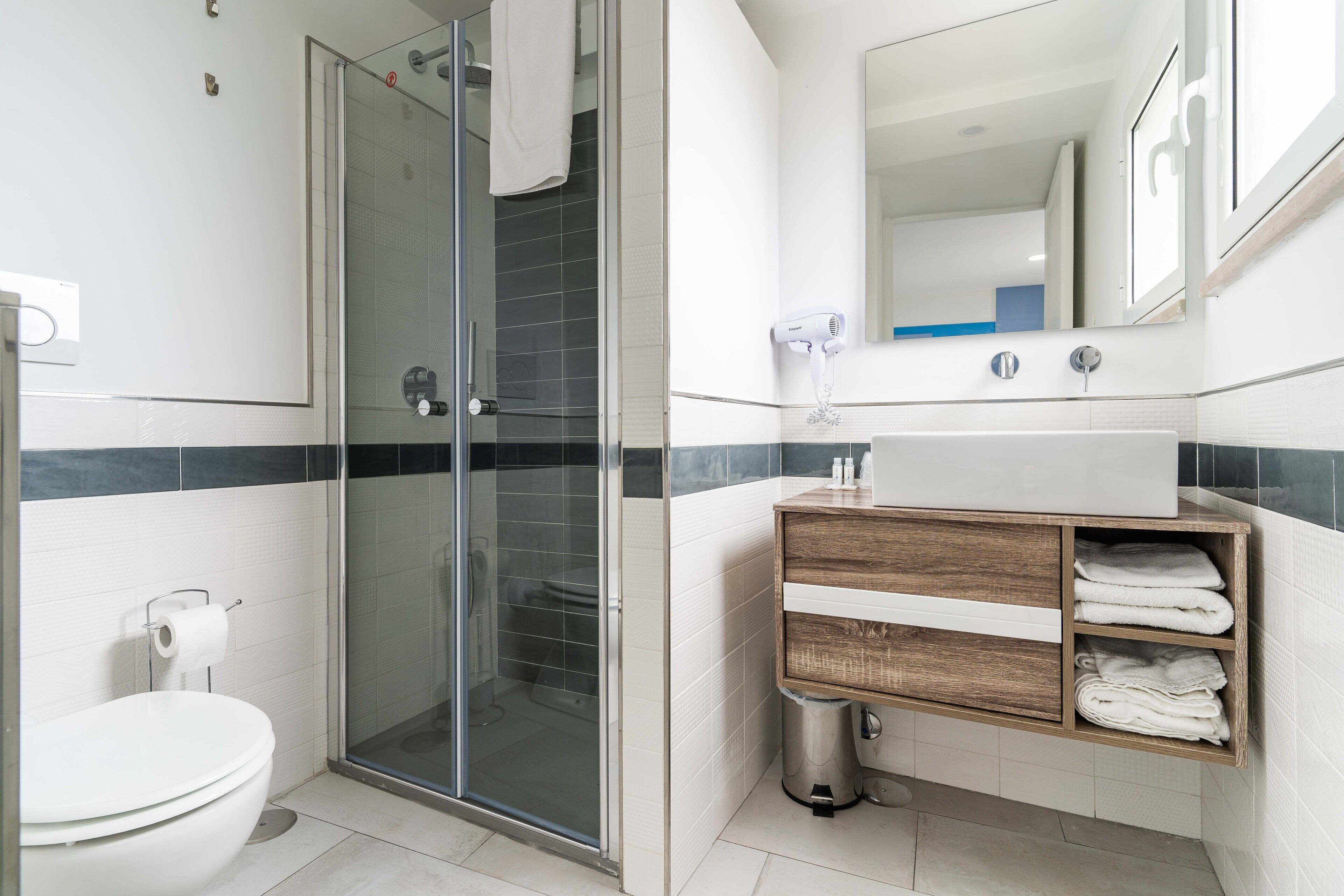 A modern bathroom with a glass shower enclosure, a white toilet, and a wooden vanity with a mirror.