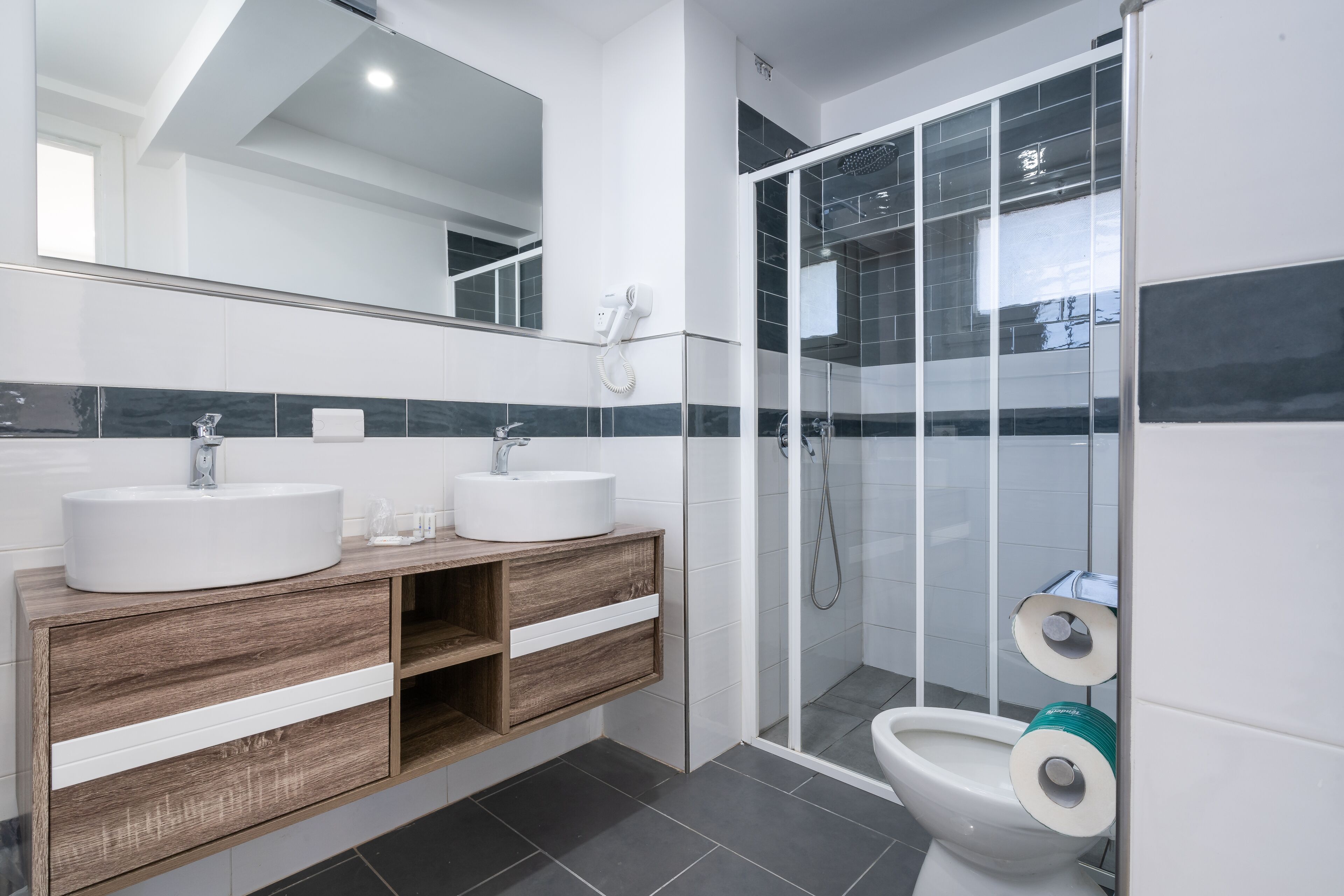 Une salle de bain moderne avec deux lavabos, un miroir et une cabine de douche.