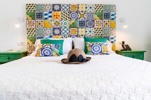 Una cama con colcha blanca, un sombrero de paja y almohadas de colores con estampados.