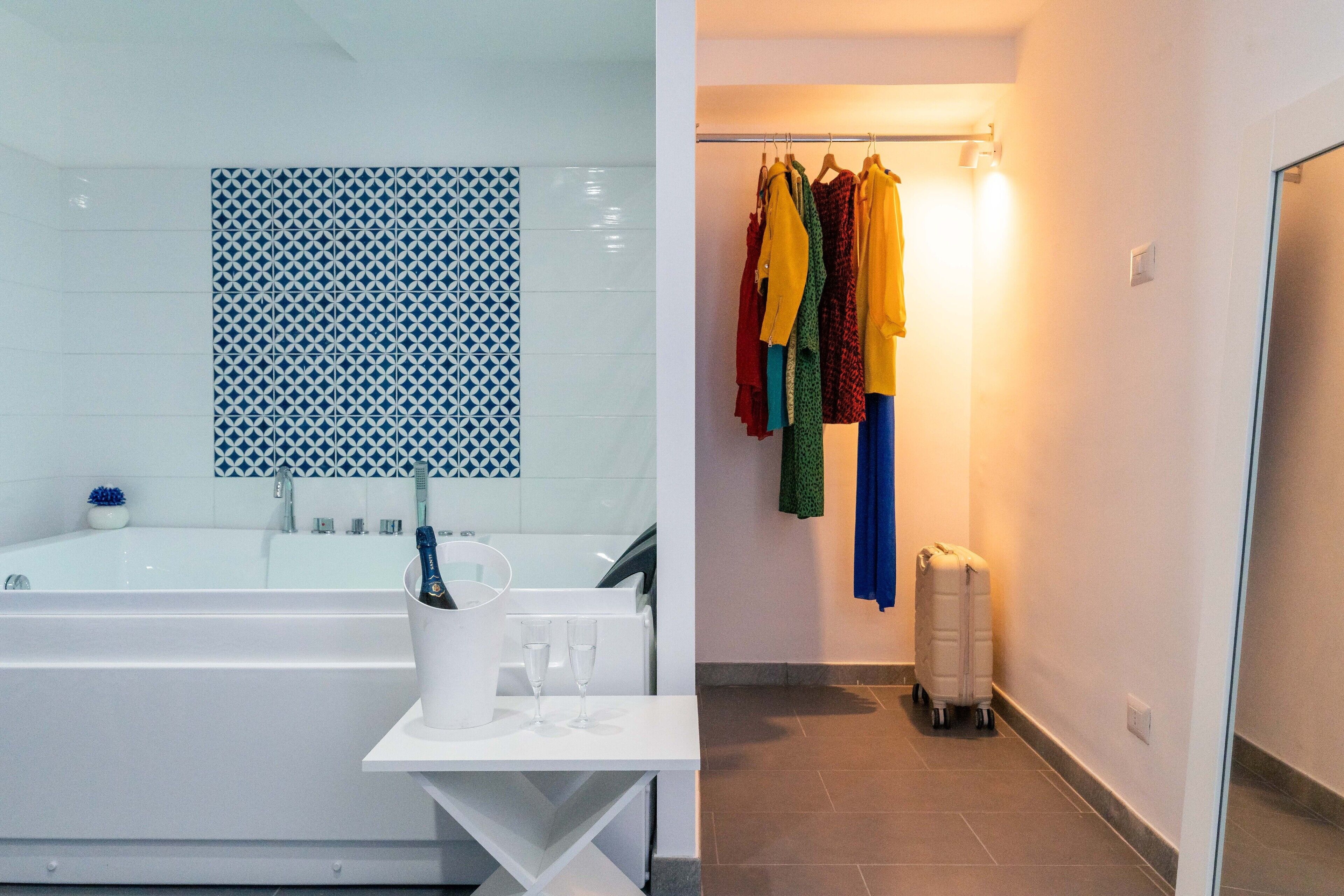 Baño con bañera, lavamanos y espejo. Hay una mesita blanca con un cepillo de dientes y un vaso de agua.