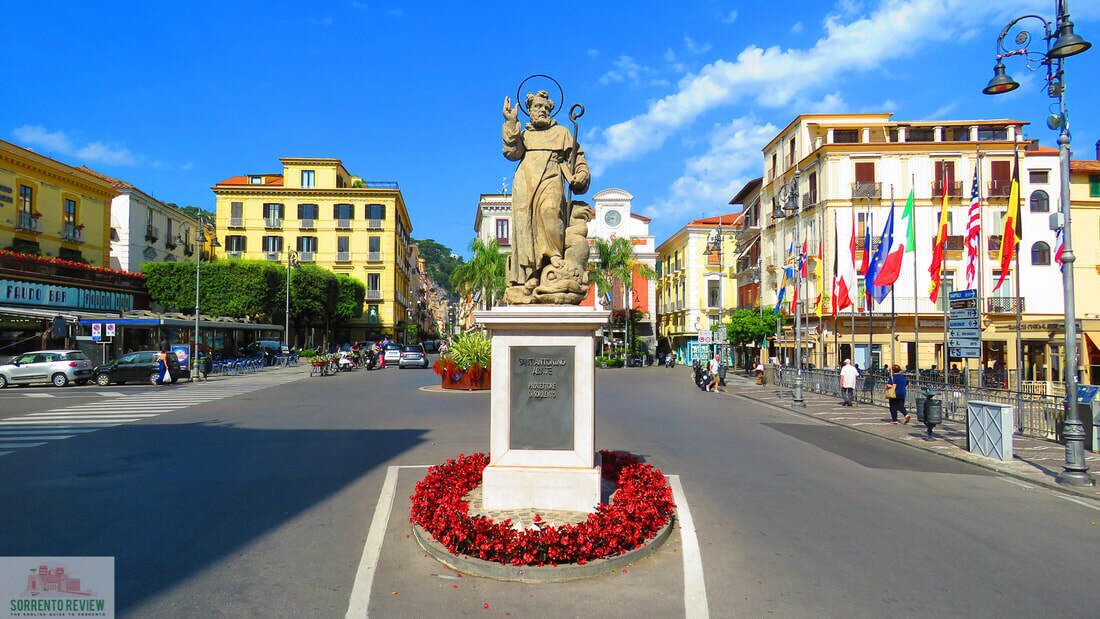A statue in a square surrounded by buildings and flags.