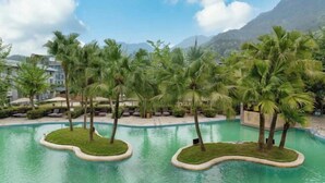 A resort pool area with palm trees and lounge chairs, surrounded by mountains.