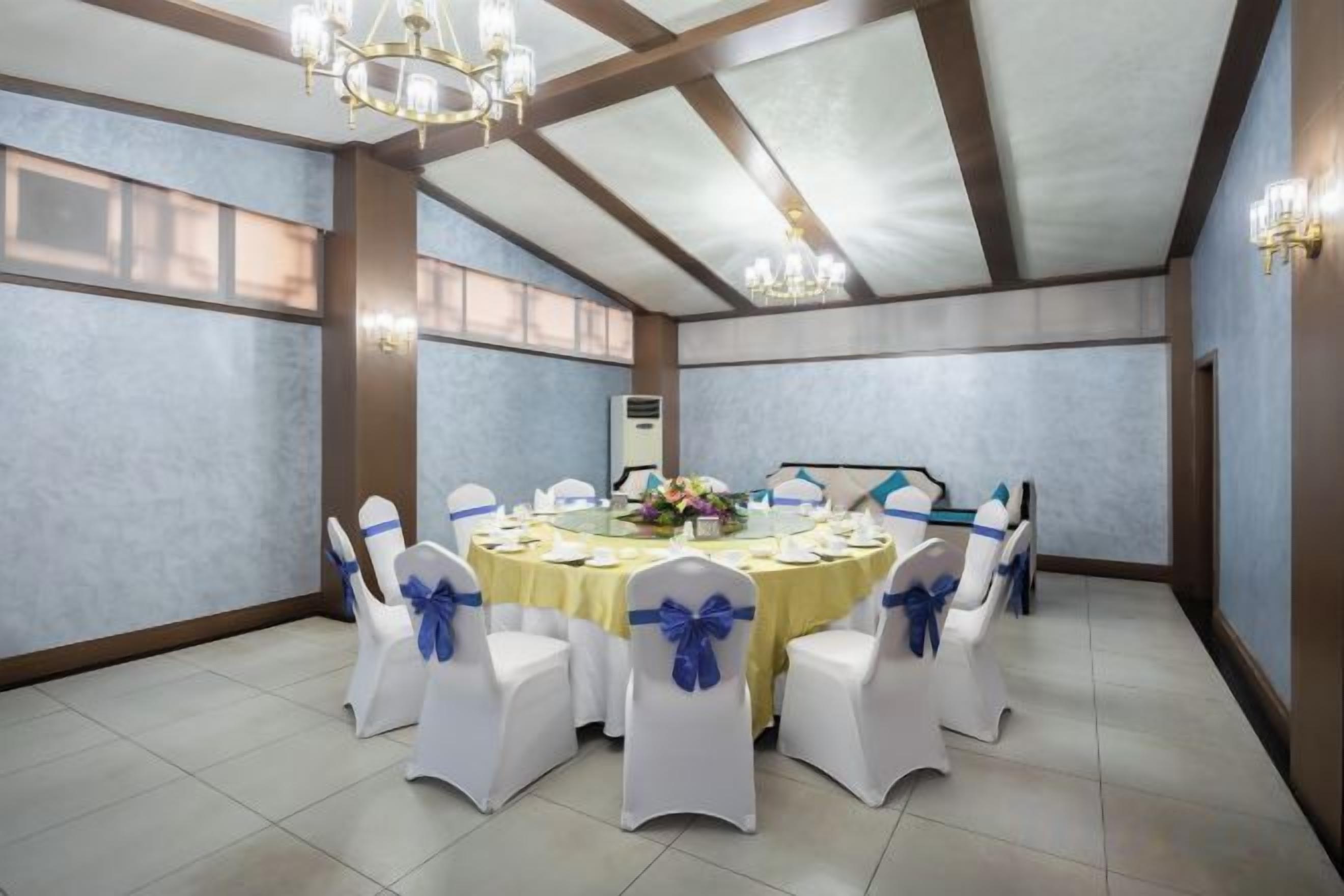 A conference room with a round table, white chairs with blue sashes, and a chandelier.
