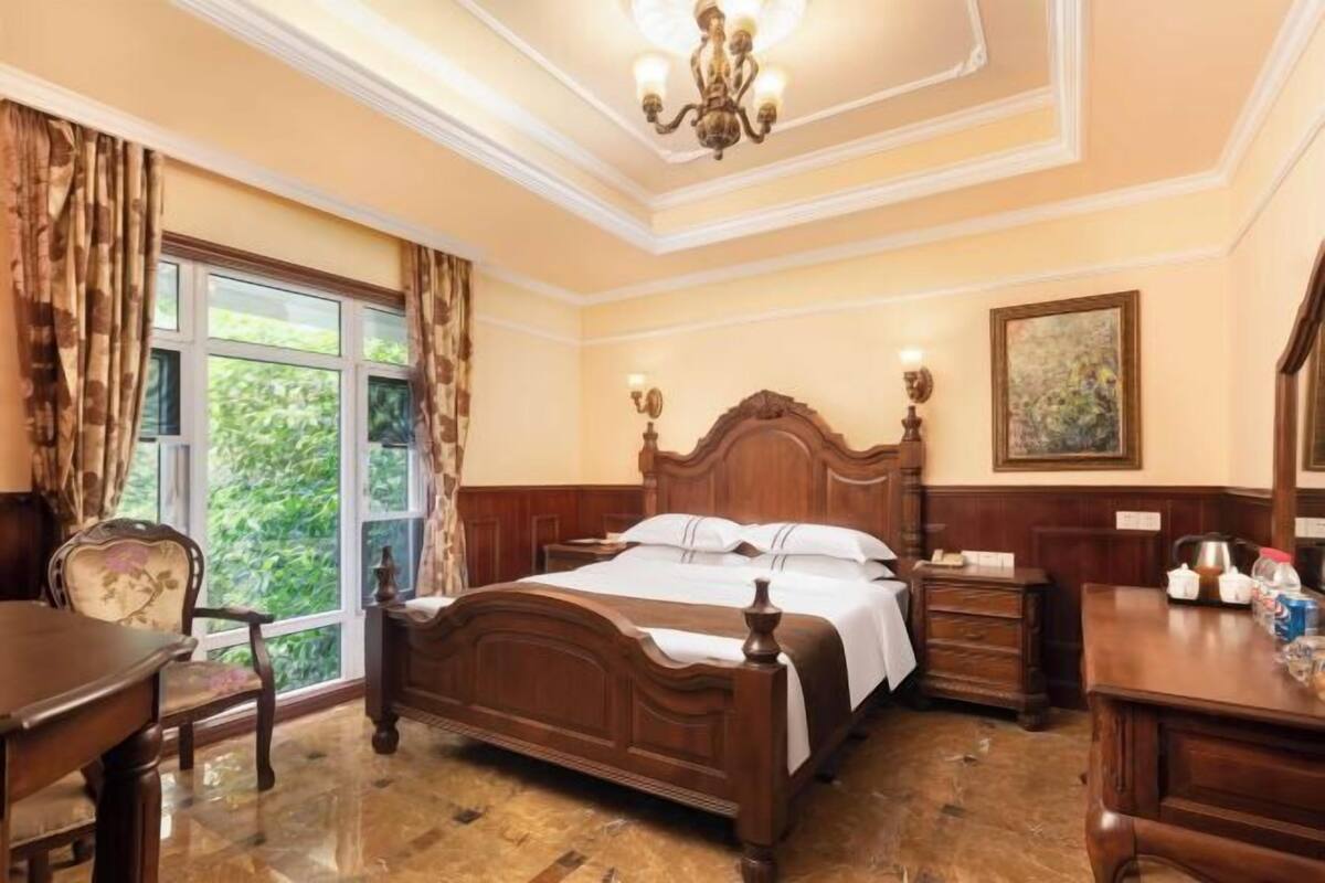 A bedroom with a wooden bed, a desk, a chair, a nightstand, and a painting on the wall.