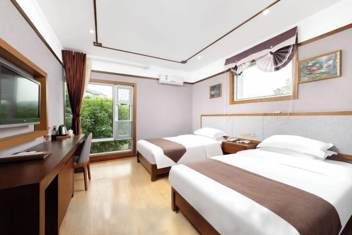 A hotel room with two beds, a desk, a chair, a TV, a window with curtains, and a painting on the wall.