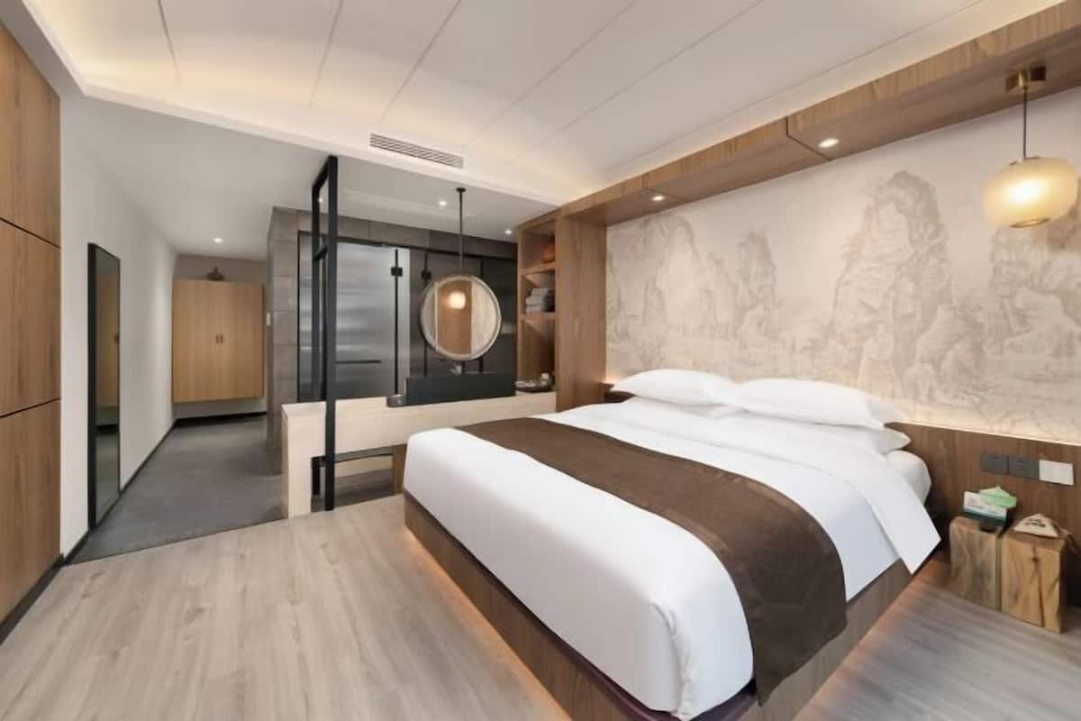 A modern hotel room with a large bed, a wooden headboard, a marble wall with a relief sculpture, and a round pendant light.