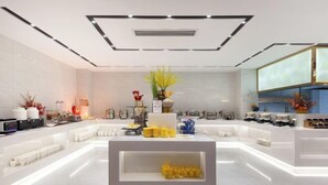 A modern, well-lit reception area with a central white counter displaying various items, surrounded by white furniture and decorative plants.