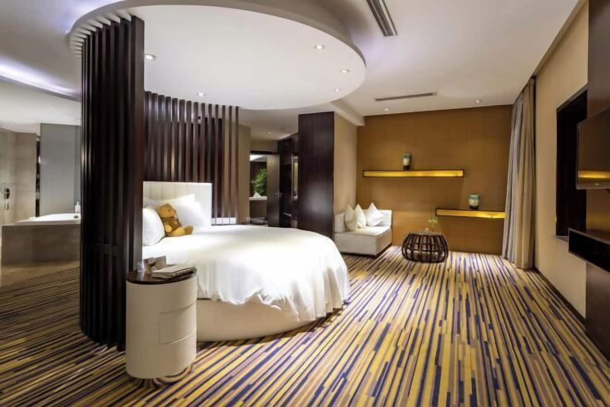 Une chambre d’hôtel moderne dotée d’un grand lit, d’une table de chevet, d’un petit coin salon et d’un téléviseur fixé au mur.