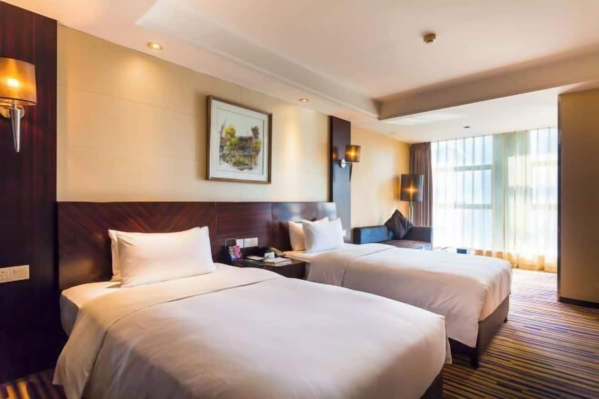 Une chambre d’hôtel avec deux lits, une grande fenêtre et un tableau au mur.
