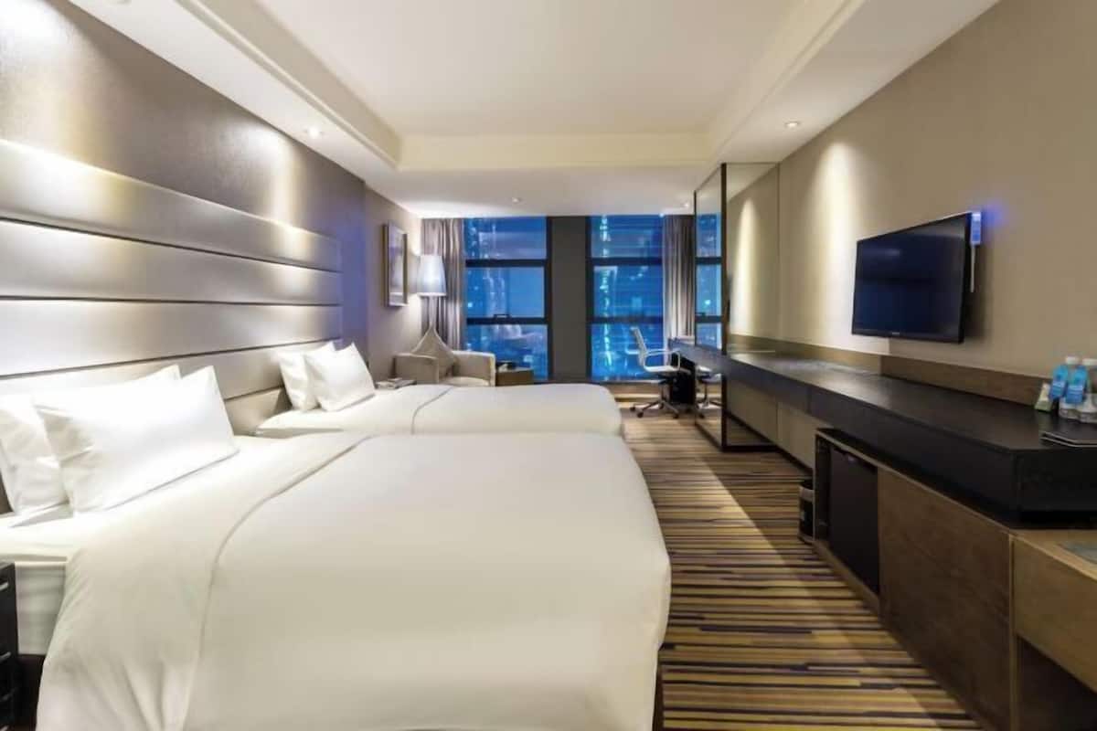 Une chambre d’hôtel avec deux lits, un bureau, une télévision et une grande fenêtre donnant sur la ville.