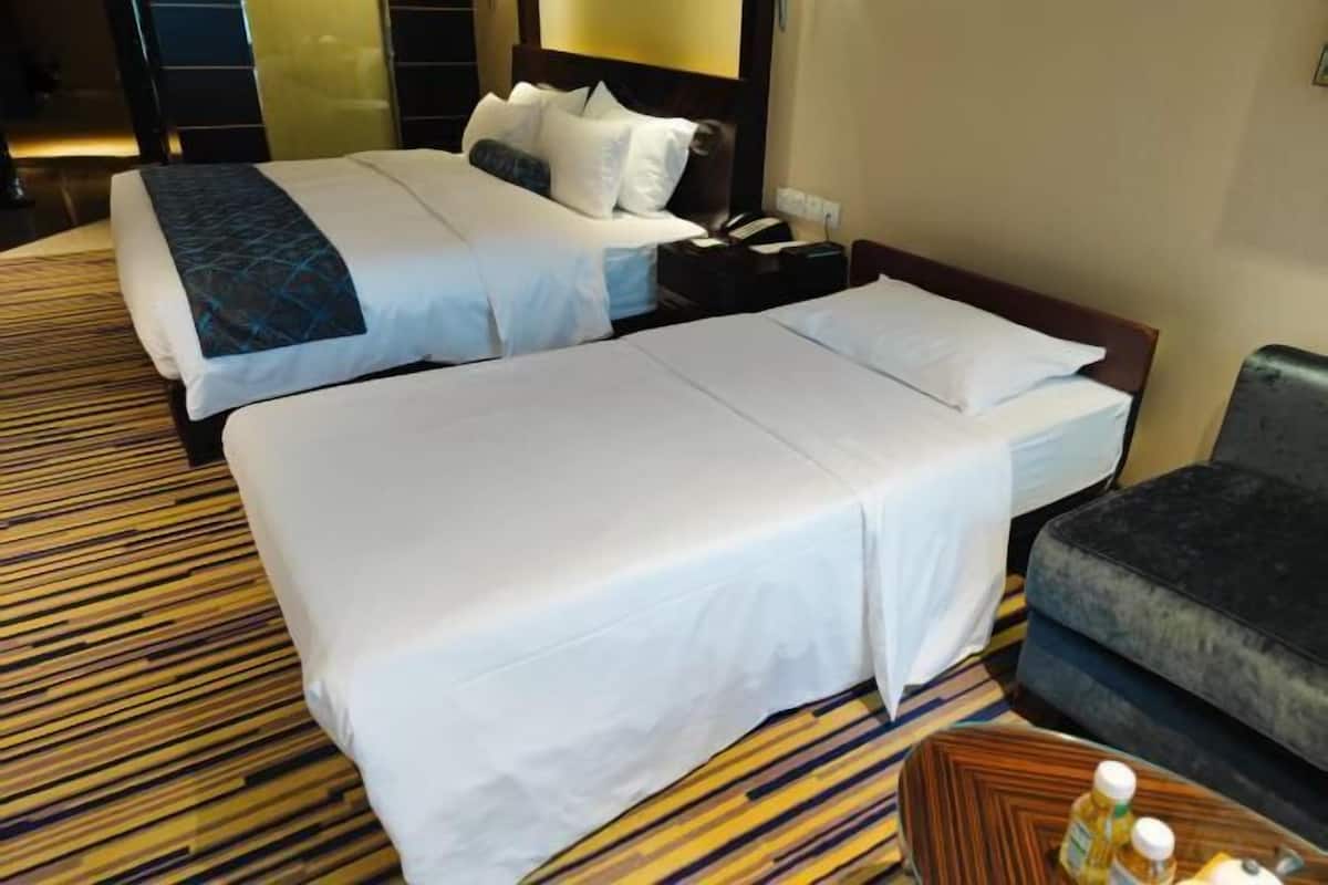 Une chambre d’hôtel avec deux lits, un canapé, une table de chevet et une moquette à motifs.