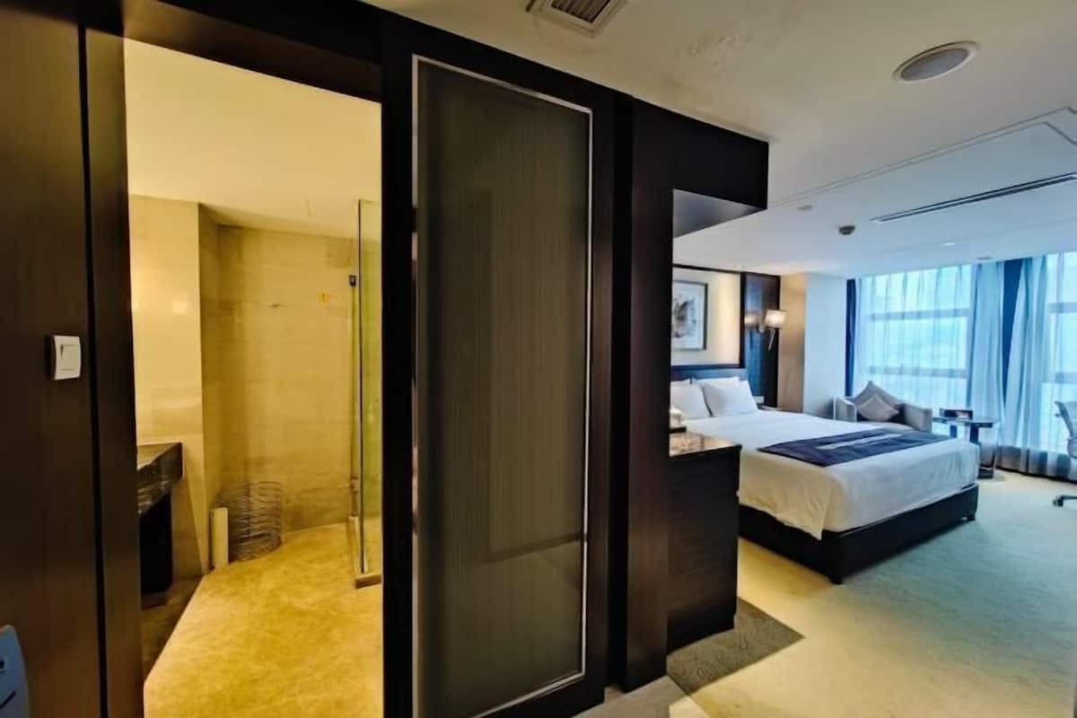 Une chambre d’hôtel comprenant un lit, un bureau, une chaise, une grande fenêtre et une porte donnant sur une salle de bain.