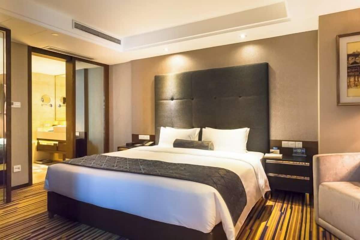 Une chambre d’hôtel avec un grand lit, une table de chevet, une chaise et une salle de bain visible à travers une porte ouverte.