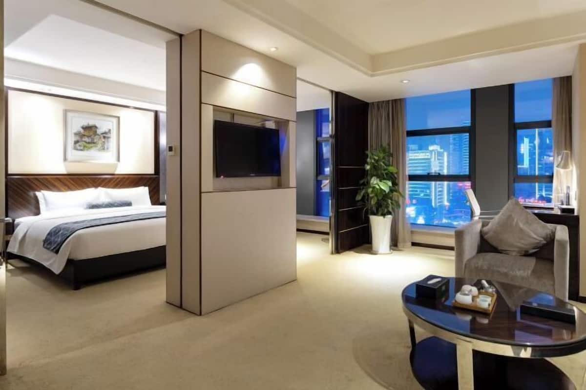 Une chambre d’hôtel comprenant un lit, une télévision, un coin salon avec une table et une grande fenêtre donnant sur la ville.